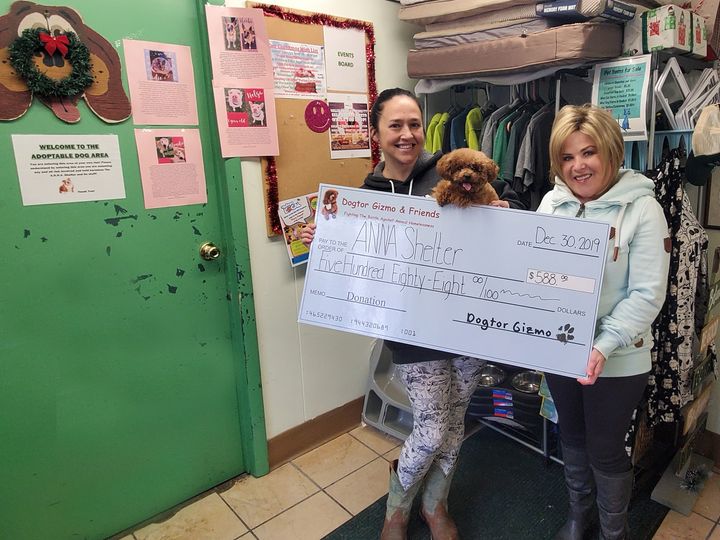 Two women holding Gizmo the dog and a donation check for the ANNA Shelter