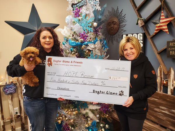 Two women holding Gizmo the dog and a donation check for H.O.P.E Rescue