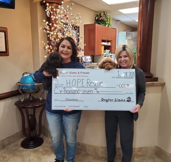 Two women holding Gizmo and Gadget the dogs and a donation check for H.O.P.E Rescue 