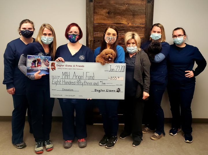 A group of people holding Gizmo the dog and a donation check for the MAH Angel Fund