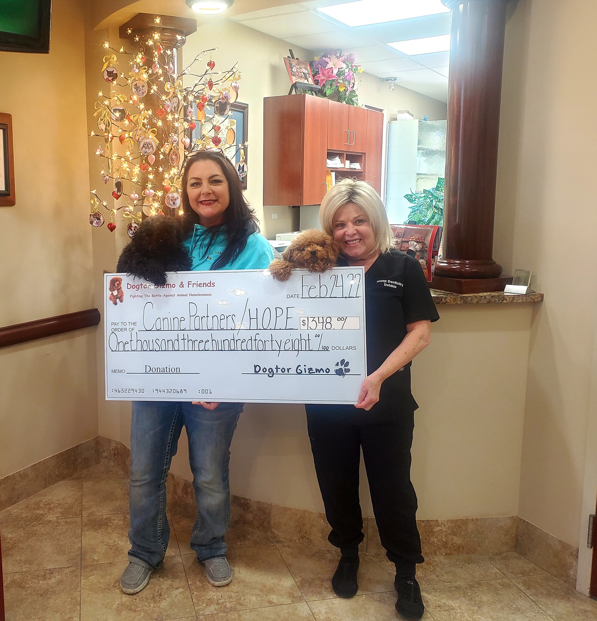 Two women holding Gadget and Gizmo the dogs and a donation check for H.O.P.E