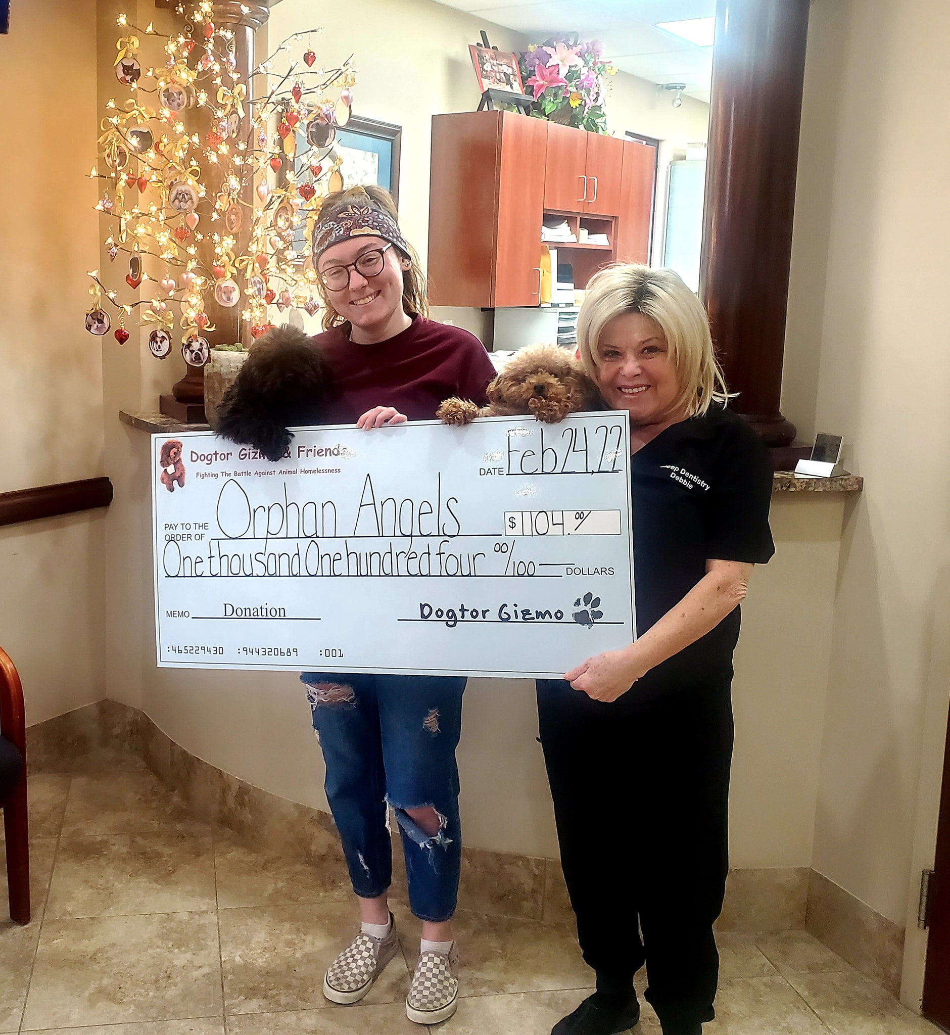 Two women holding Gizmo and Gadget the dogs and a donation check for Orphan Angels 