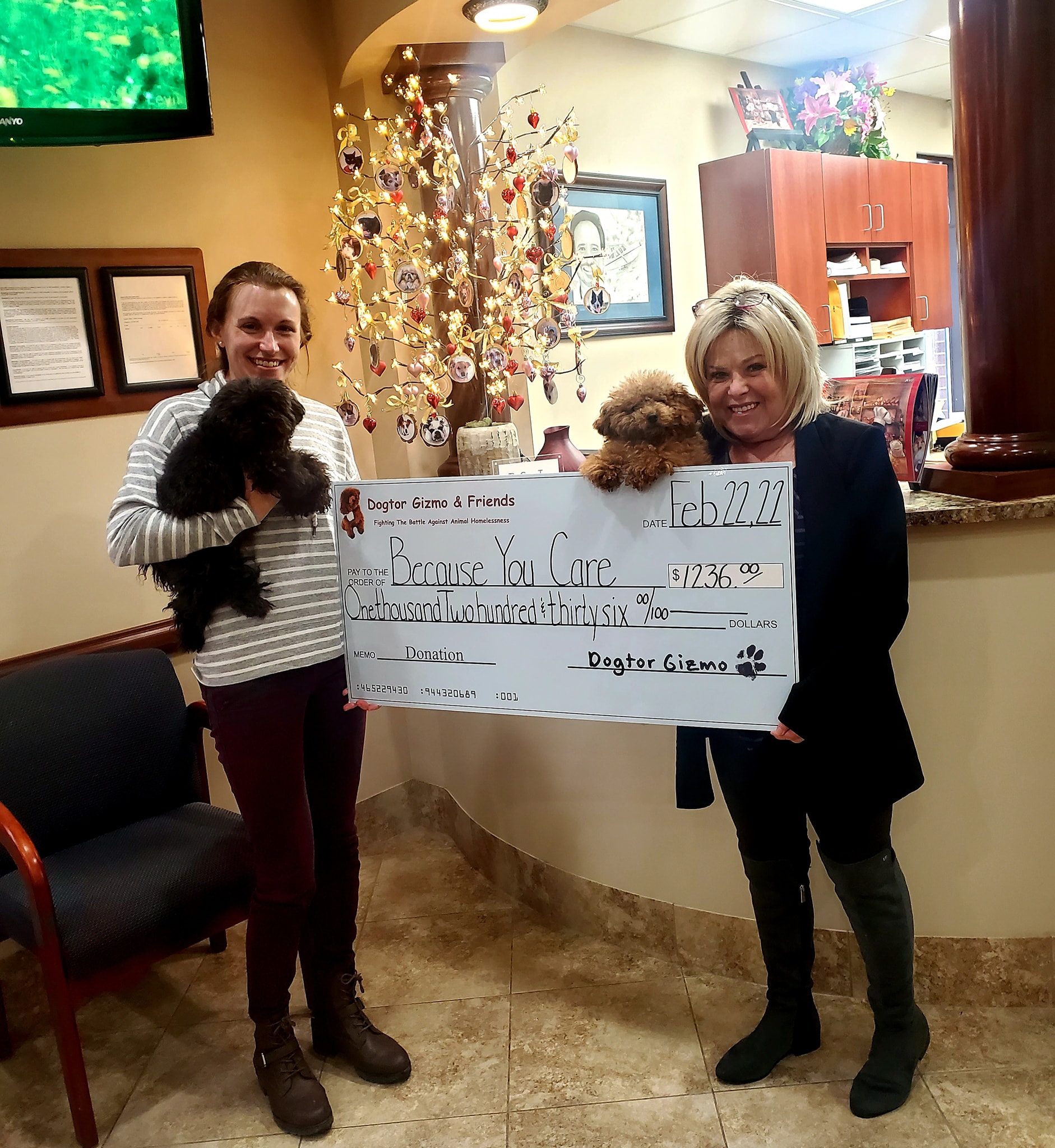 Two women holding Gizmo and Gadget the dogs and a donation check for Because You Care 