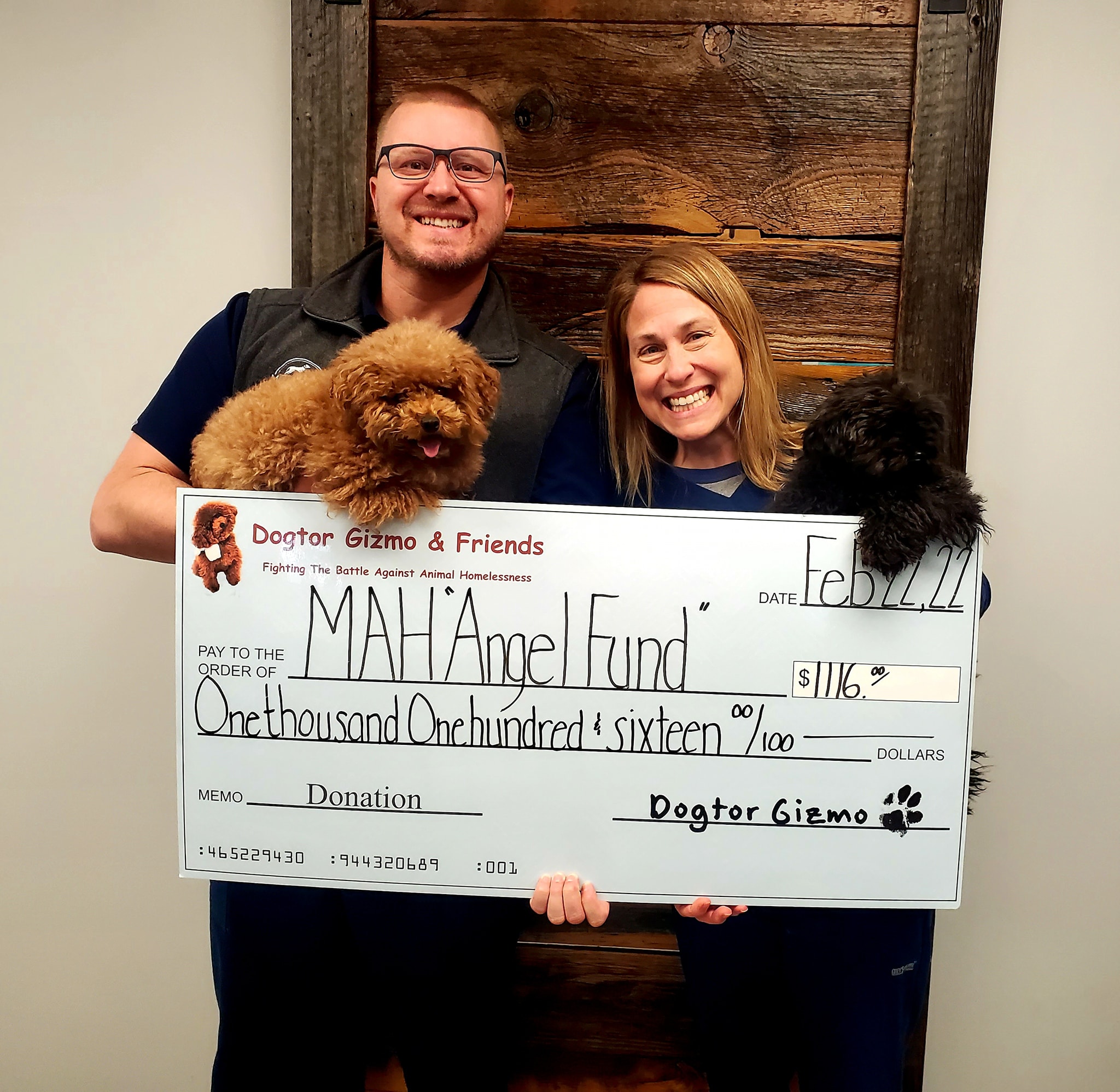 A man and woman holding Gizmo and Gadget the dogs and a donation check for MAH Angel Fund 