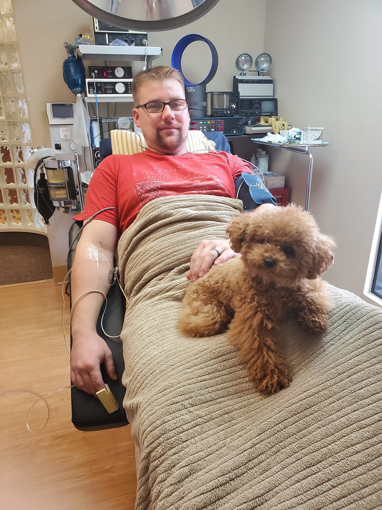 A bearded man on the examination chair with Gizmo the dog in his lap