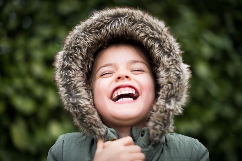 A laughing child in a winter coat. The hood is pulled up 