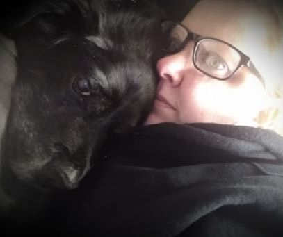 A person in glasses snuggling with a black dog
