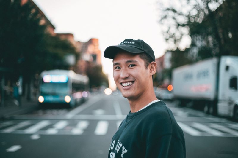 A smiling man in a baseball cap, standing in front of a crosswalk